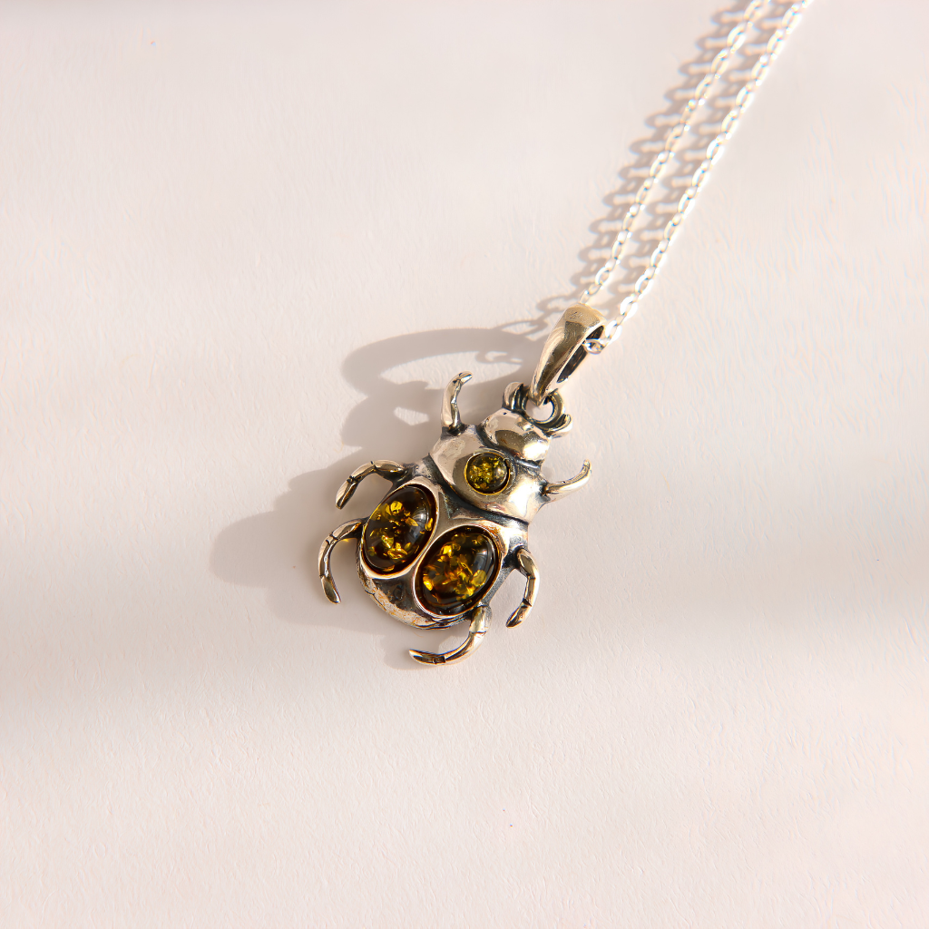 A silver beetle pendant amber necklace with two round yellow gemstones, shown on a matching silver chain against a plain off-white background.