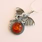 Silver dragon pendant with amber stone on a light pink background