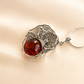 amber necklace with spider web design and red gemstone on a beige background