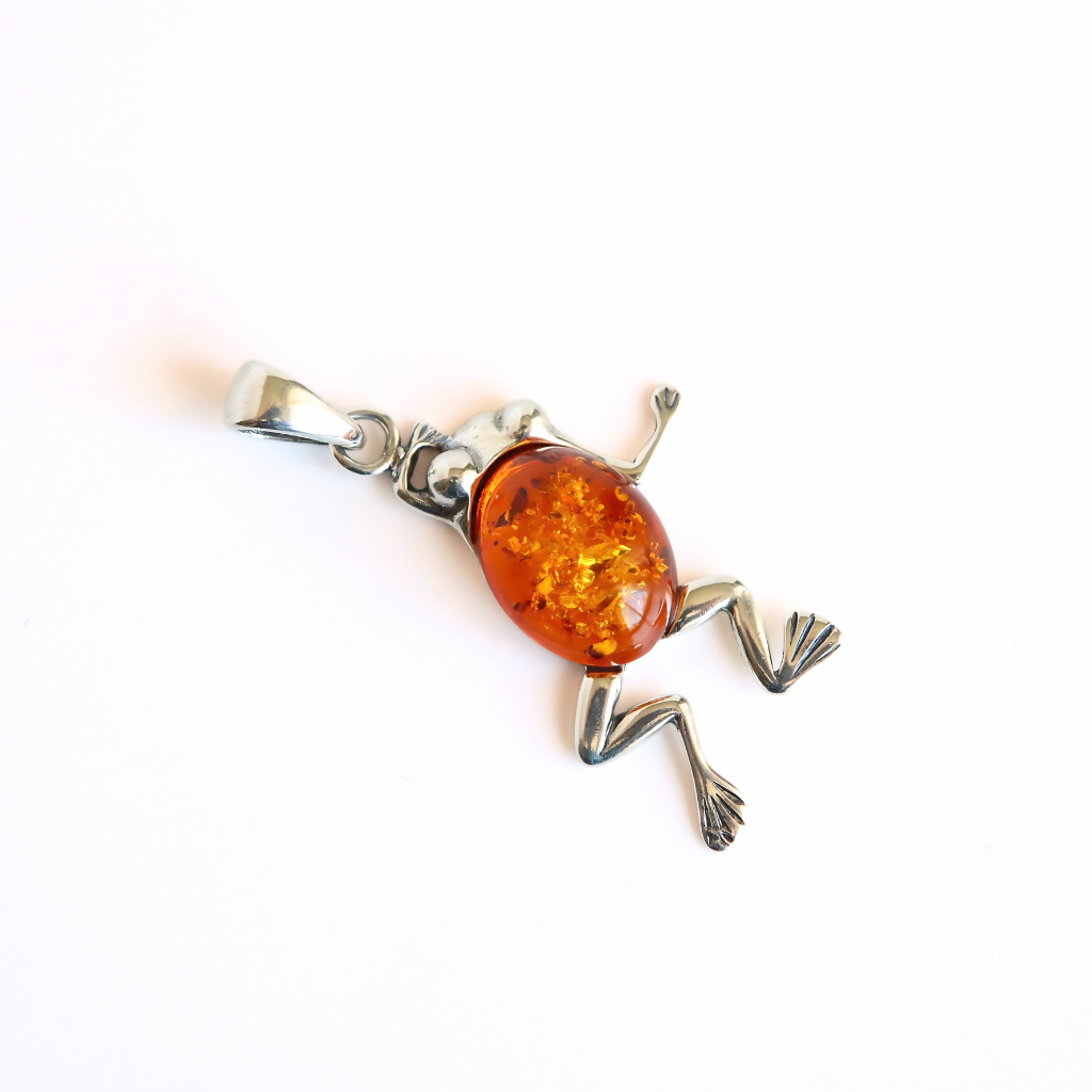A frog-shaped pendant necklace featuring a polished amber-colored oval center stone and silver-toned metal legs, feet, and bail, photographed on a plain white background.