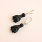 Black amber bat earrings on a beige background