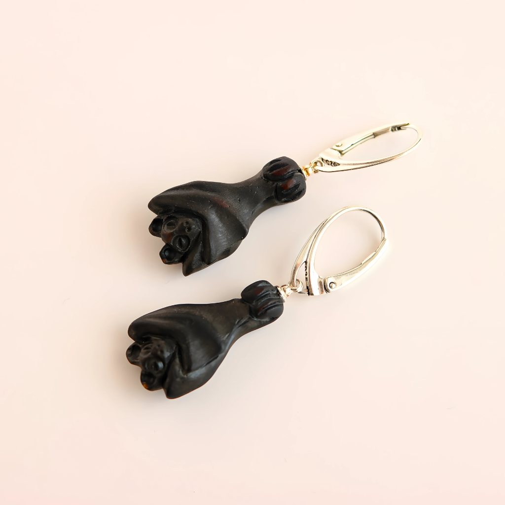 Black amber bat earrings on a beige background