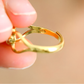 Gold amber ring held between fingers against a beige background