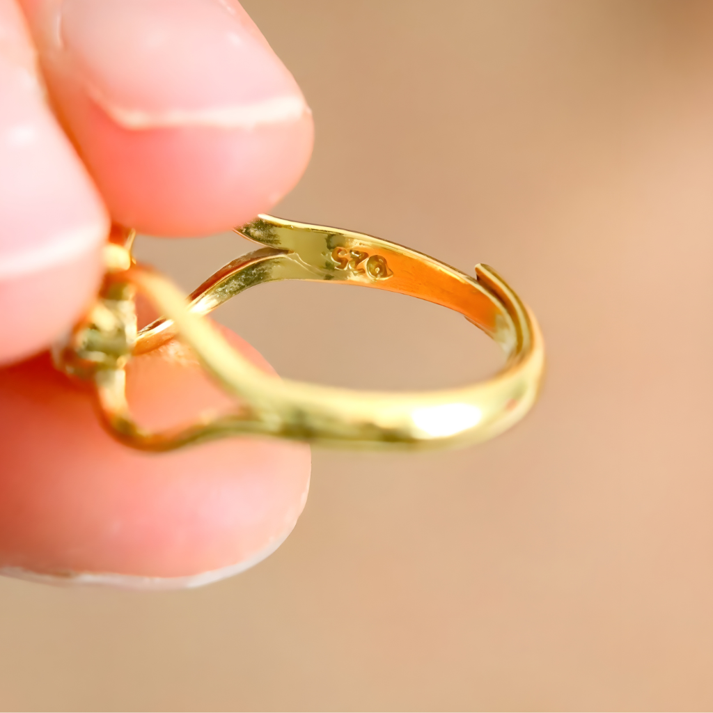 Gold amber ring held between fingers against a beige background