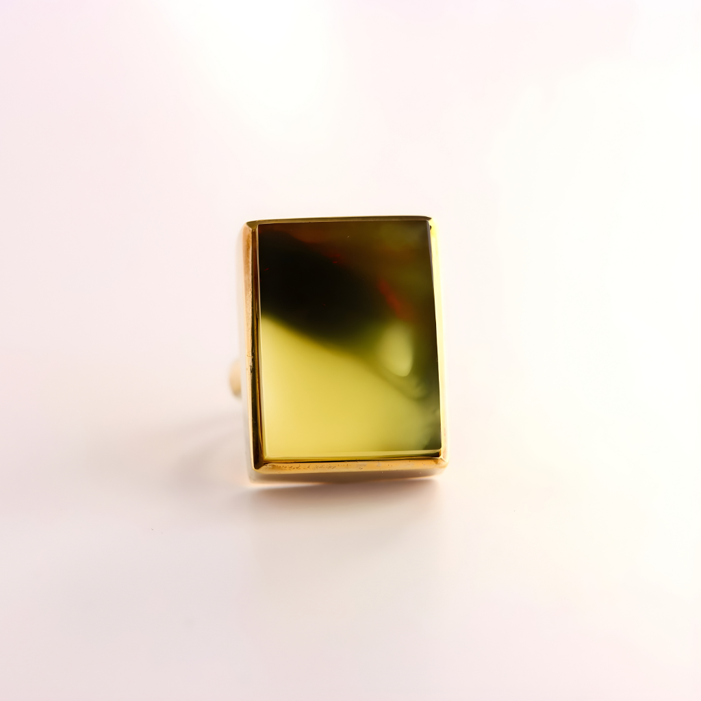 Gold amber ring with a rectangular green gemstone on a light pink background
