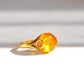 A gold ring featuring a large, polished Baltic amber gemstone , photographed on a clean white surface with soft shadows.