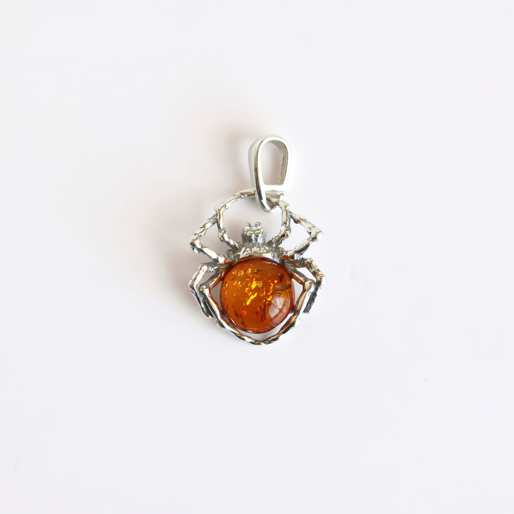 A amber spider-shaped silver pendant featuring a polished amber-colored gemstone in the center, set against a plain white background.