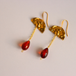 A pair of gold drop earrings featuring textured gold components and dangling vintage Lucite amber-red teardrop beads, shown on a light neutral background.