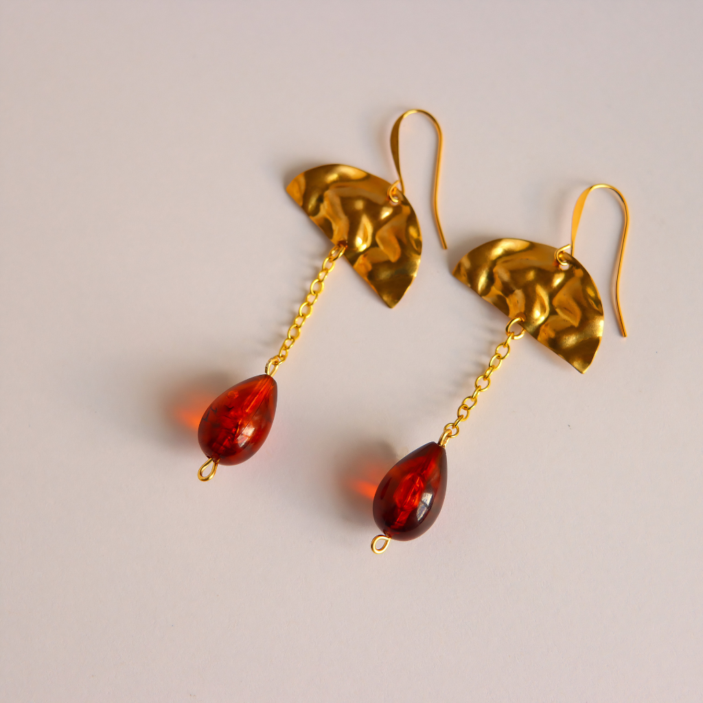 A pair of gold drop earrings featuring textured gold components and dangling vintage Lucite amber-red teardrop beads, shown on a light neutral background.