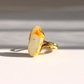 A gold white amber ring with a large, irregularly shaped cream-colored stone featuring orange-brown edges, photographed on a white surface with soft diagonal shadows.