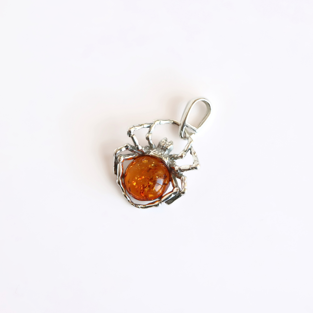 A polished amber spider pendant featuring eight spider legs centered on a clean off-white background.