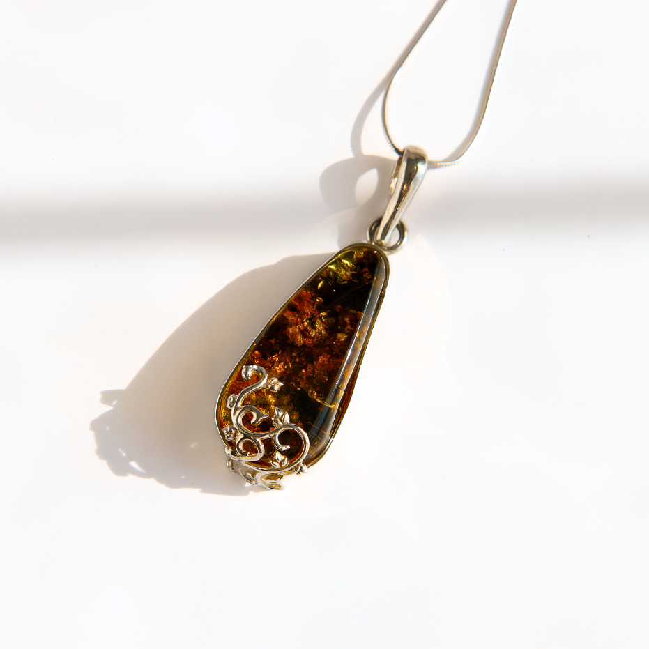 A teardrop-shaped green amber pendant necklace with a silver-toned filigree accent at the bottom, suspended on a silver chain against a bright white background.