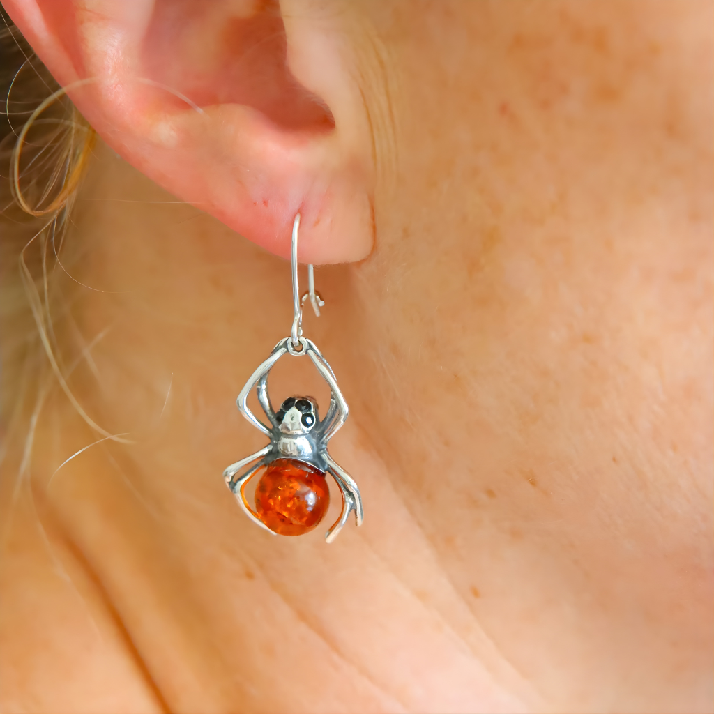 Spider-shaped sterling silver earrings with amber bead worn on an ear