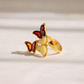 A gold amber butterfly ring with cream-colored amber wings and red accents, photographed on a warm, light beige background with soft shadows.
