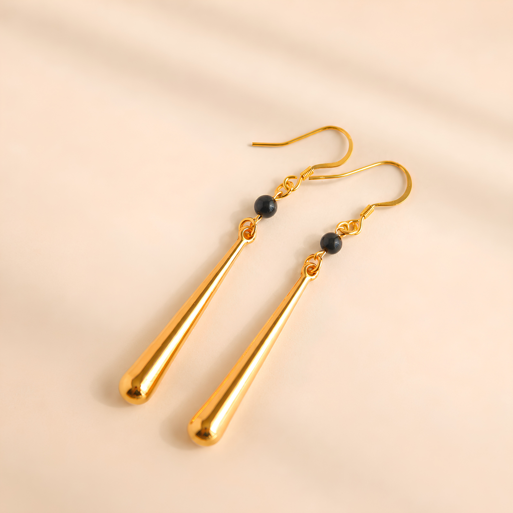 Gold drop earrings with black beads on a beige background