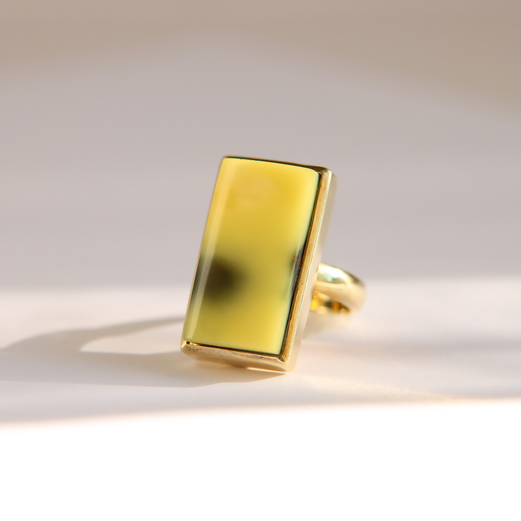 A gold  Baltic amber ring featuring a large, polished rectangular yellow stone, photographed on a clean, light beige background with soft shadows.