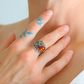 Hand wearing a sterling silver ring with an orange gemstone, finger with blue floral tattoos.