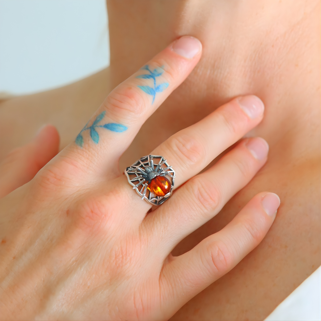Hand wearing a sterling silver ring with an orange gemstone, finger with blue floral tattoos.