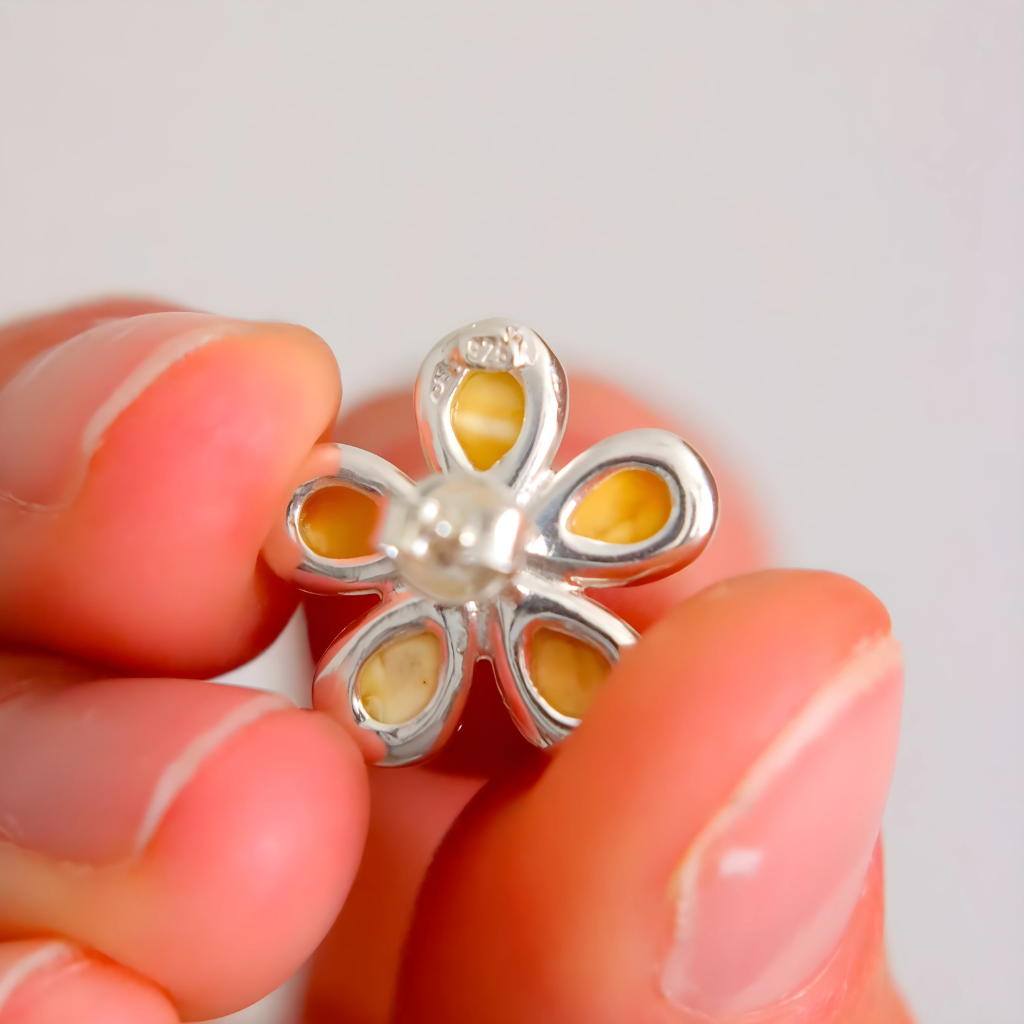 Silver flower-shaped stud earrings with yellow center held between fingers against a light background