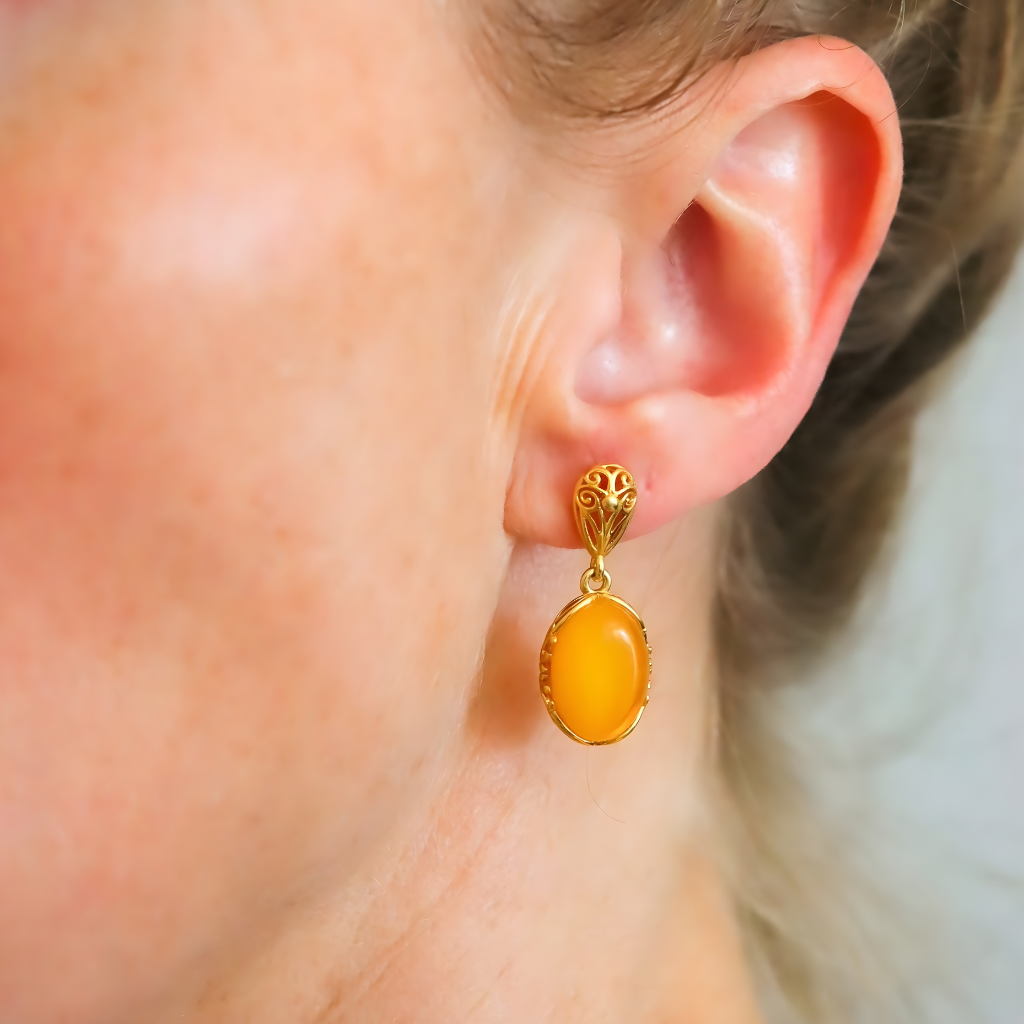 Gold earrings with amber stone worn by a person