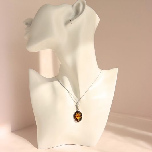 A silver-toned amber scarab necklace with an oval amber pendant displayed on a white ceramic mannequin bust against a soft beige background.