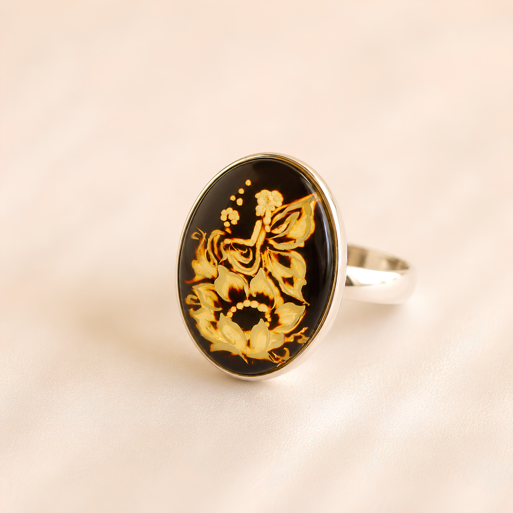 An oval amber cameo ring featuring a black background with a detailed gold floral and butterfly design, set in a polished silver-tone band.