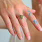 Hand wearing an amber ring with a green gemstone on a blurred background