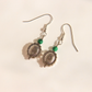 A pair of silver-toned western malachite dangle earrings with circular wheel-like charms, small green beads, and fishhook wires, photographed on a plain light background.