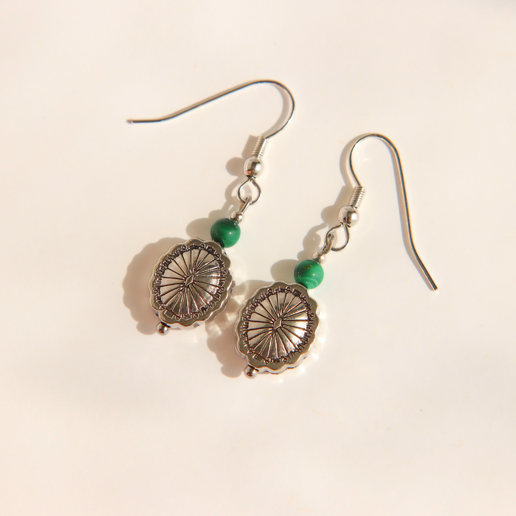 A pair of silver-toned western malachite dangle earrings with circular wheel-like charms, small green beads, and fishhook wires, photographed on a plain light background.