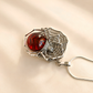 Silver spider amber necklace with a red gemstone and spider web design on a beige background