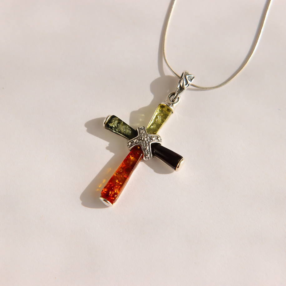 A silver amber cross pendant necklace featuring four colored inlay segments: orange, black, olive green, and light green, with a small silver detail at the center, shown on a plain light background.