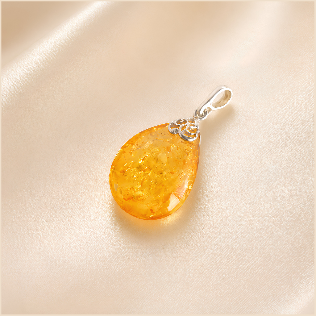 Teardrop-shaped amber pendant with silver chain on a beige background