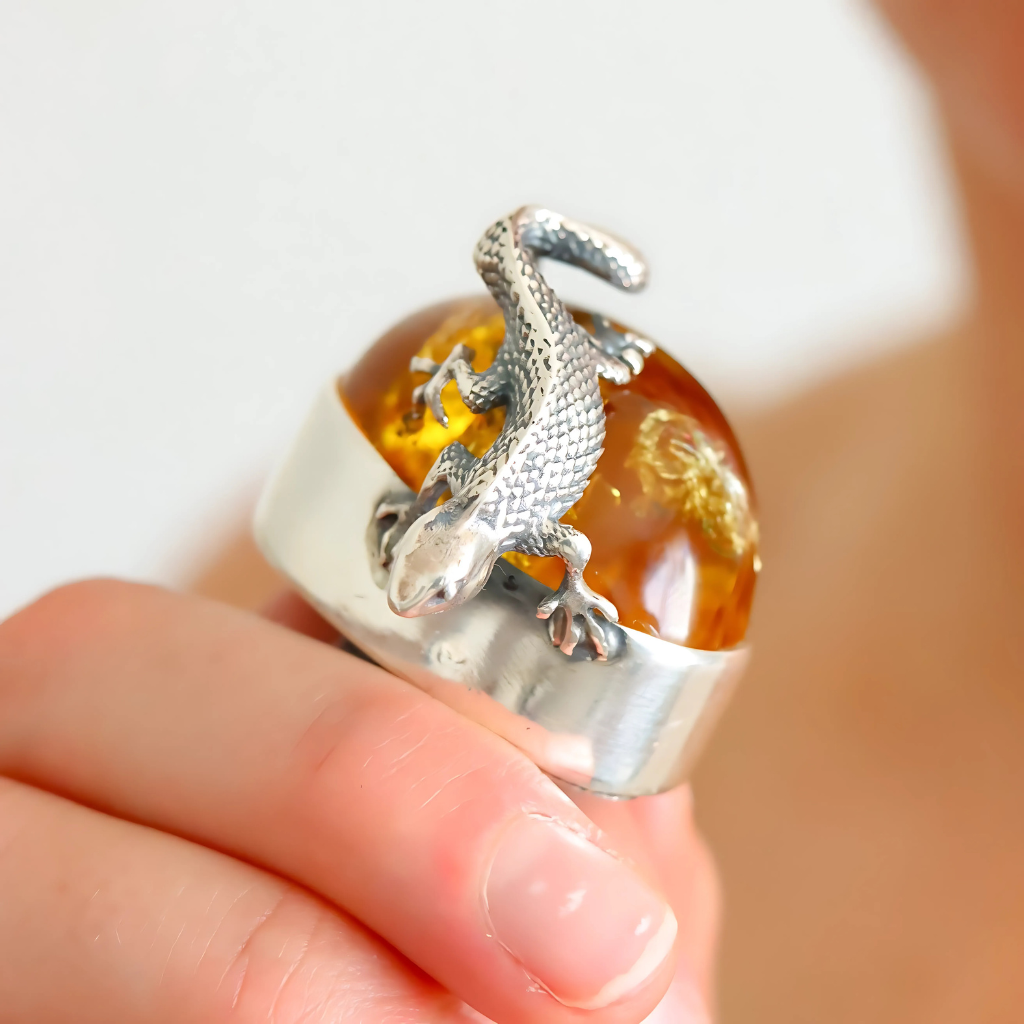 Silver statement ring with a lizard design on a transparent sphere held by a hand.