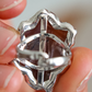 Close-up of a silver flower ring held between fingers with a blurred background