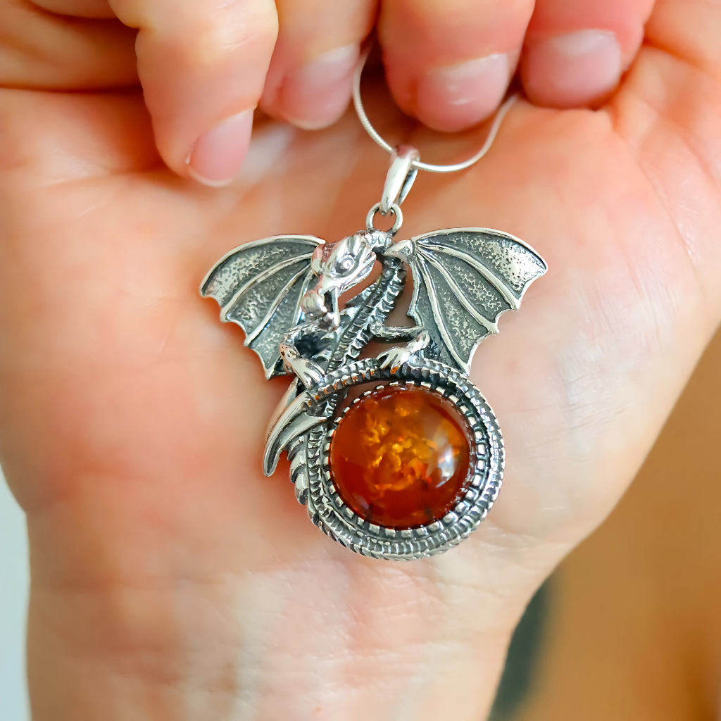 Silver dragon pendant with amber stone held in a hand