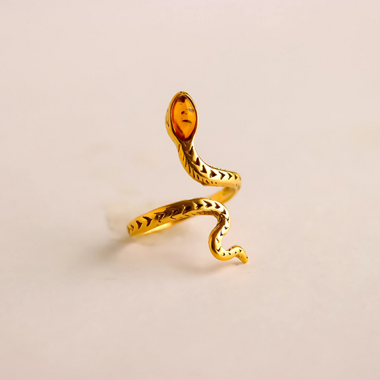 Gold snake ring with a amber stone on a beige background