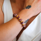 Close-up of a wrist wearing a pink Botswana agate bracelet with maroon and gold beads.