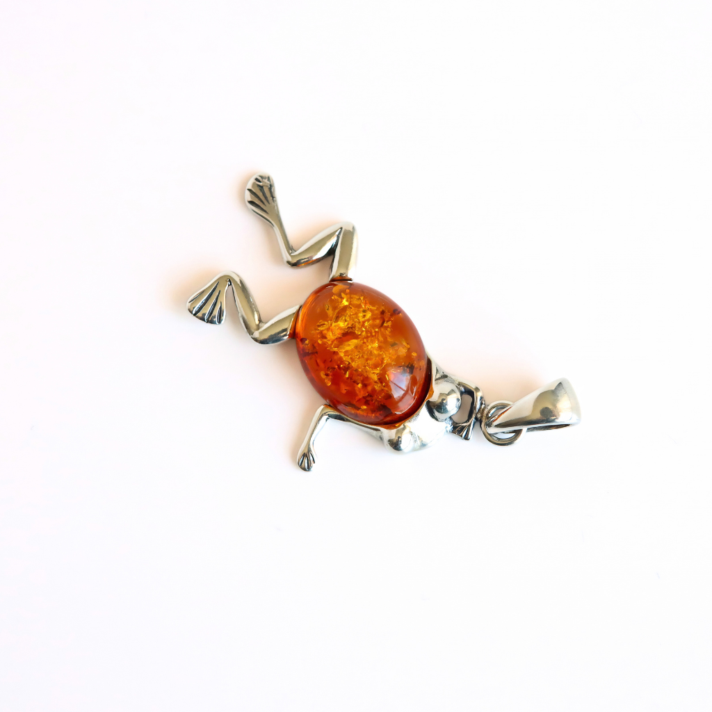A frog-shaped silver pendant necklace with a polished amber-colored glass or resin belly, photographed on a plain white background.