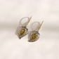 A pair of silver filigree drop amber earrings with marquise-cut green gemstones, displayed on a light cream background.