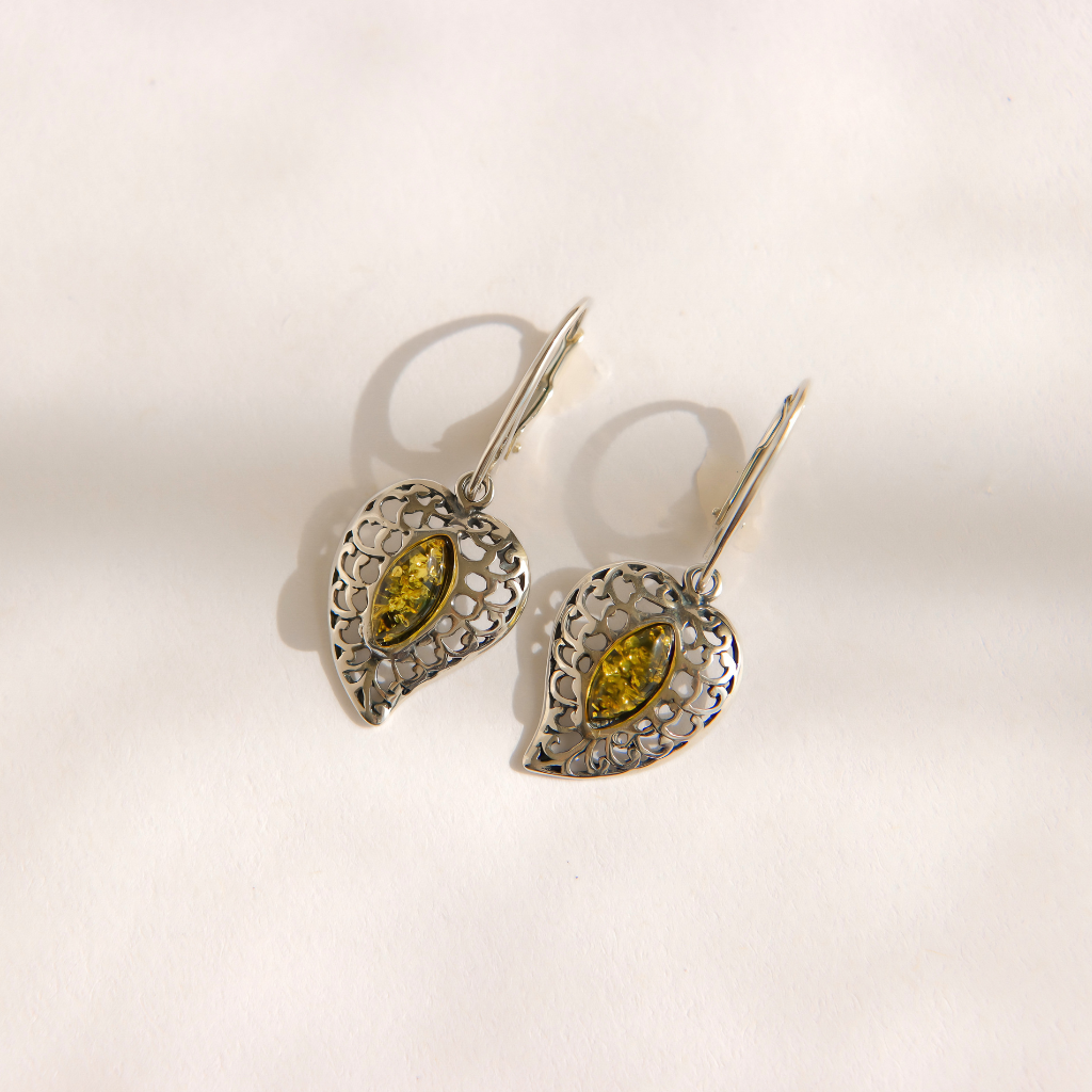 A pair of silver filigree drop amber earrings with marquise-cut green gemstones, displayed on a light cream background.
