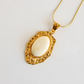 Gold amber necklace pendant with a white stone on a light gray background