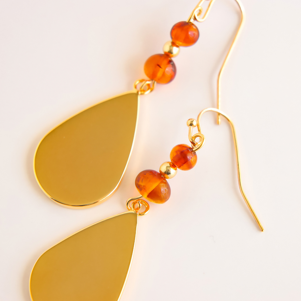 close up of gold drop earrings with amber gemstones on white background