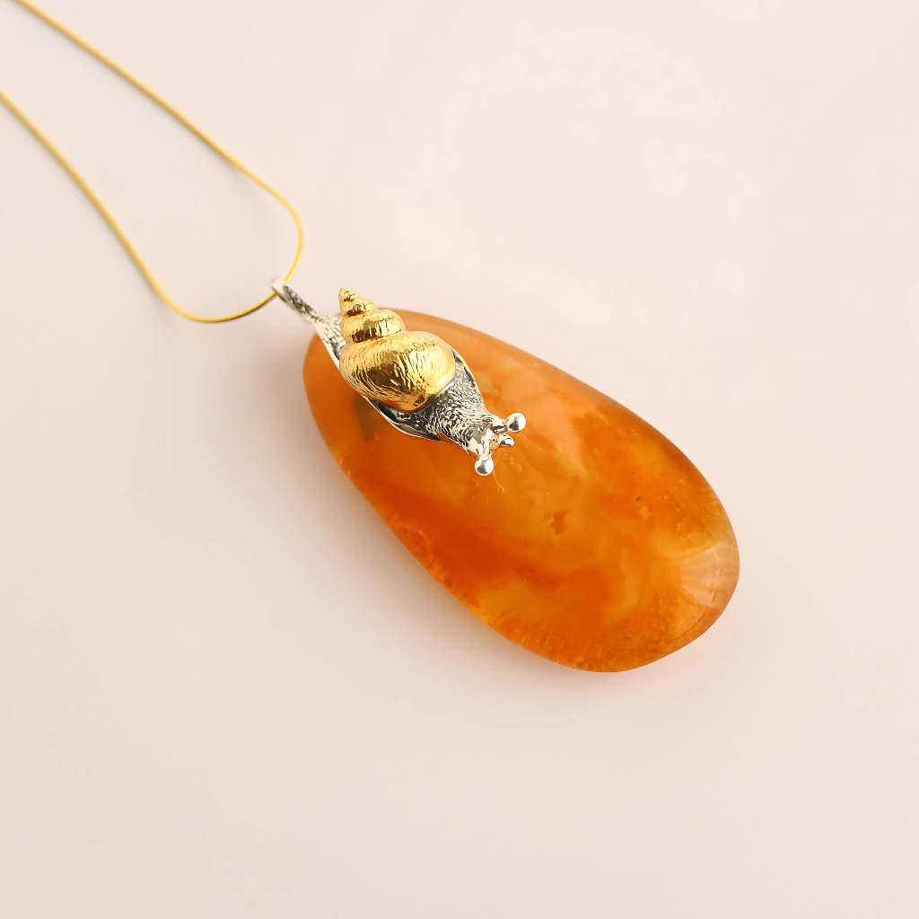 Orange teardrop-shaped pendant statement necklace with gold and silver accents on a beige background
