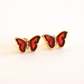Butterfly-shaped gold stud earrings with red wings and gold frames on a white background