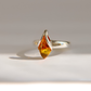 A silver amber ring featuring a marquise-cut amber gemstone, photographed on a clean, light gray surface with a soft shadow.