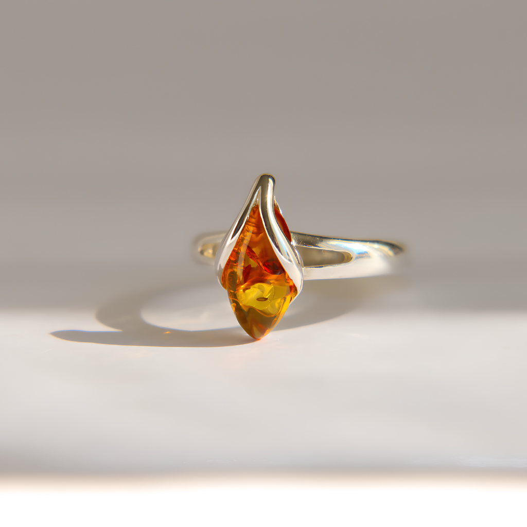 A silver amber ring featuring a marquise-cut amber gemstone, photographed on a clean, light gray surface with a soft shadow.
