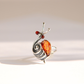A silver Baltic amber snail ring with a polished amber-orange shell and small red eye accents, photographed on a clean white background with a soft shadow.