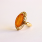 Gold amber ring with an orange stone on a light background