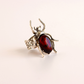 A silver scarab ring with a large, polished dark red oval gemstone on a light cream background.