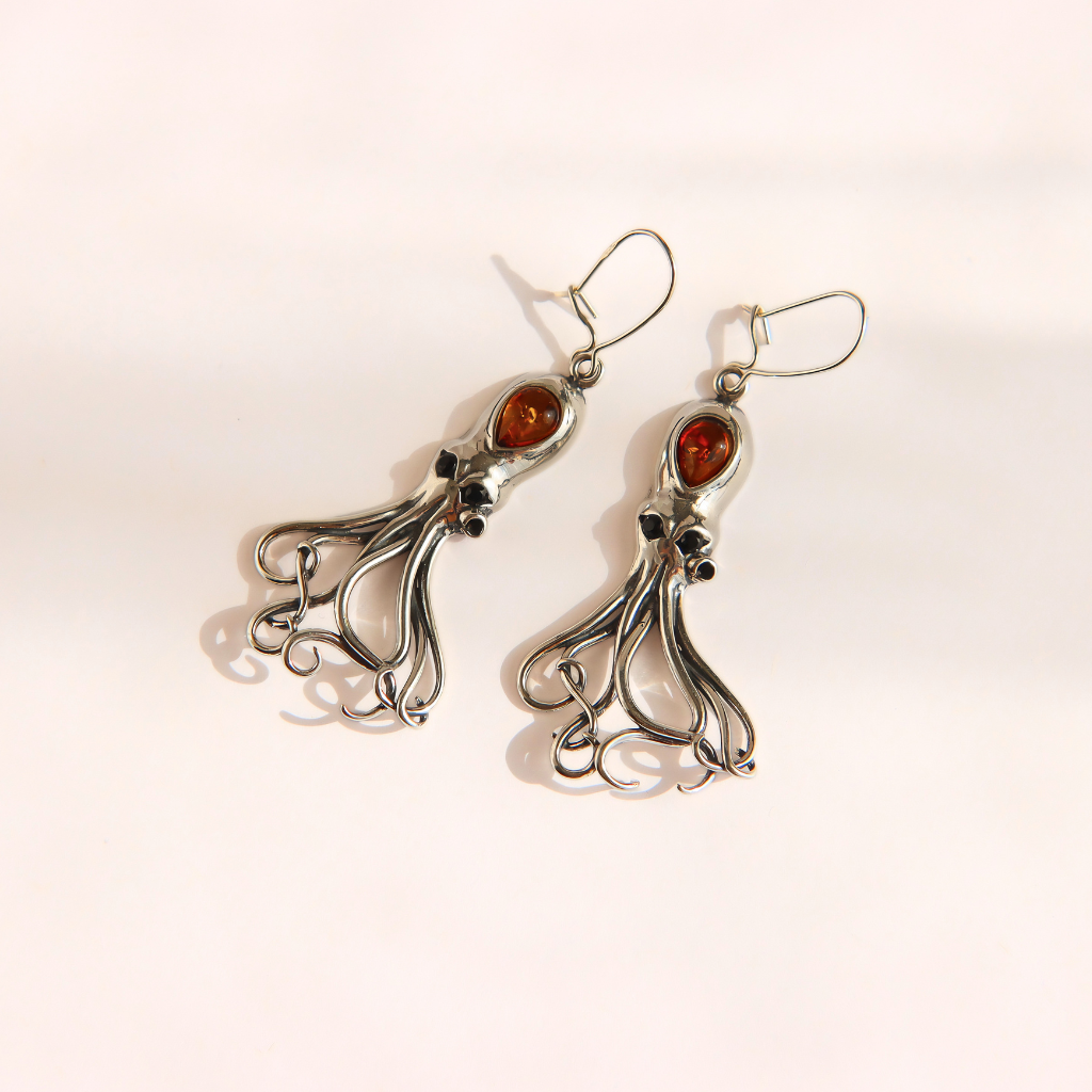 A pair of silver-toned dangle amber octopus earrings with intricate curled tentacle-like wire details and oval amber-colored stone accents, photographed on a plain light background.